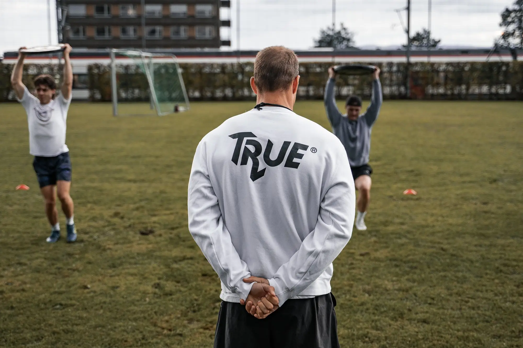 TRUE coach watching a team during athletic training on a sports field